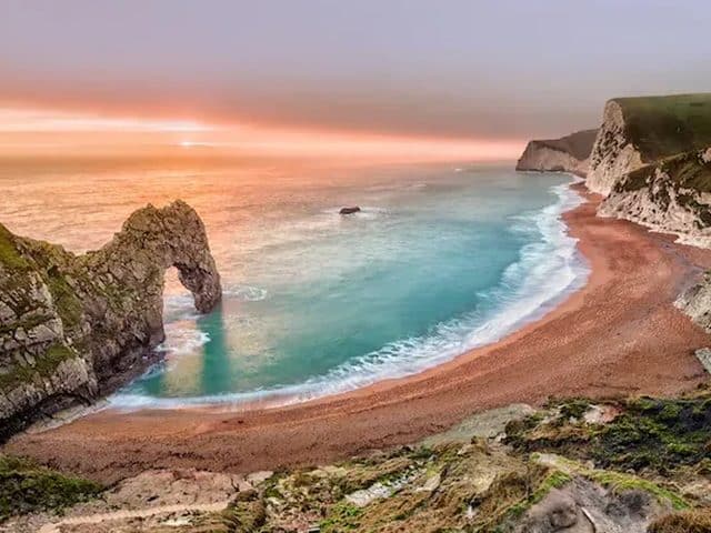 Durdle Door arch at sunset with waves lapping on a sandy beach